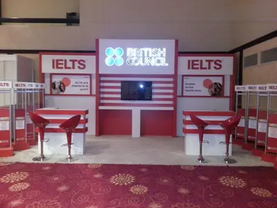 British Council IELTS — stand de feria — módulos repetidos en hilera, rojo (la unidad ya instalada)