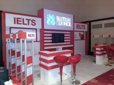 British Council IELTS — stand de feria — módulos repetidos en hilera, blanco (la unidad ya instalada)