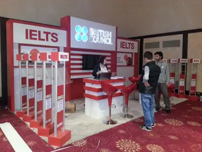British Council IELTS — stand de feria — asientos tapizados, blanco (la unidad ya instalada)