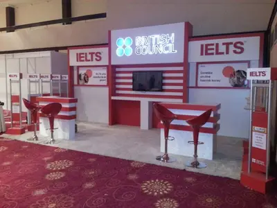 British Council IELTS — stand de feria — módulos repetidos en hilera, pantalla plana montada (en una sala de eventos)