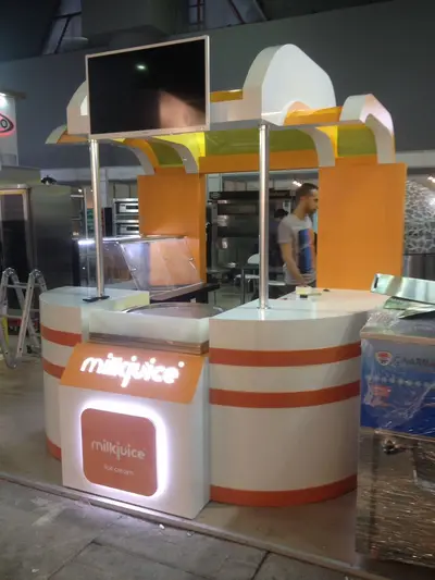 Milk Juice — fuar standı — süpürgen kanat formlu kanopi, turuncu (sahada montaj)